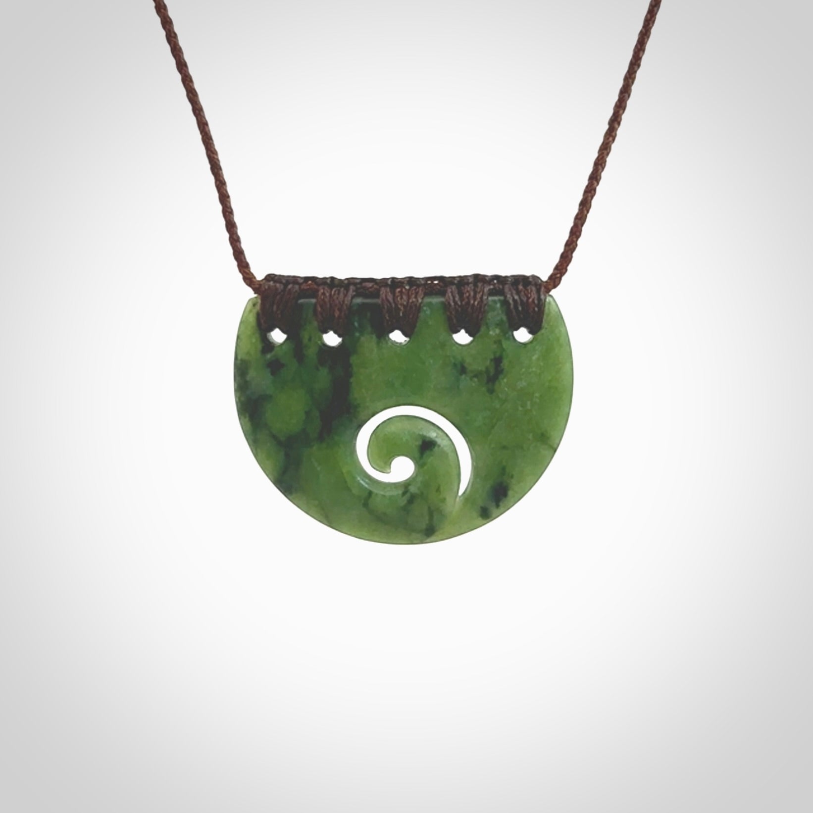 This picture shows a small hand carved jade contemporary half-shield pendant with koru heart. It is a deep green and is a wonderful, delicate piece of jewellery. The cord is hand plaited and adjustable so that you can position the pendant where it suits you best. This piece was carved for us by Kyohei Noguchi. Delivery is free worldwide.