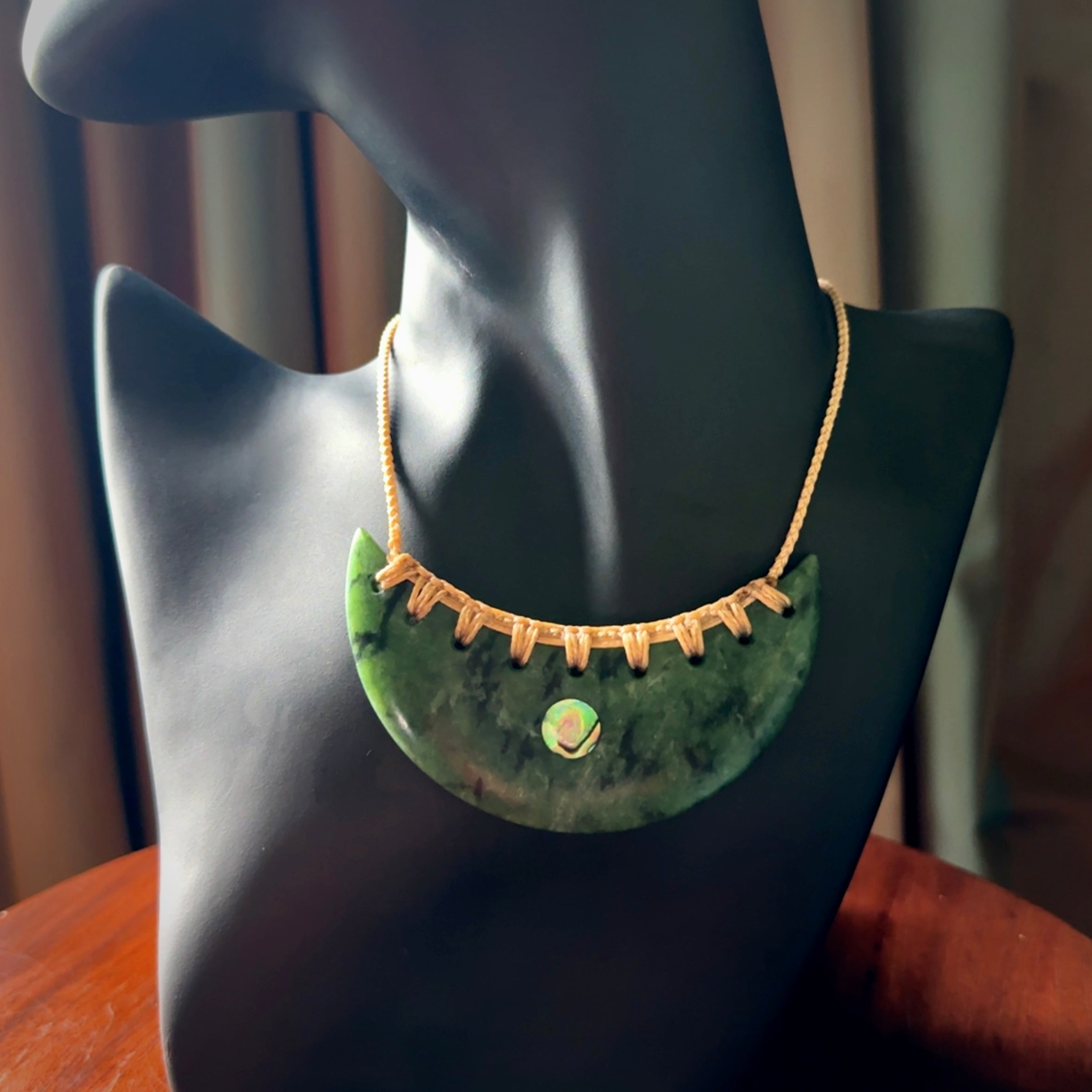 This picture shows a large hand carved jade contemporary half-shield pendant with Paua Shell inlay. It is a deep green and is a wonderful, delicate piece of jewellery. The cord is hand plaited and adjustable so that you can position the pendant where it suits you best. This piece was carved for us by Kyohei Noguchi. Delivery is free worldwide.