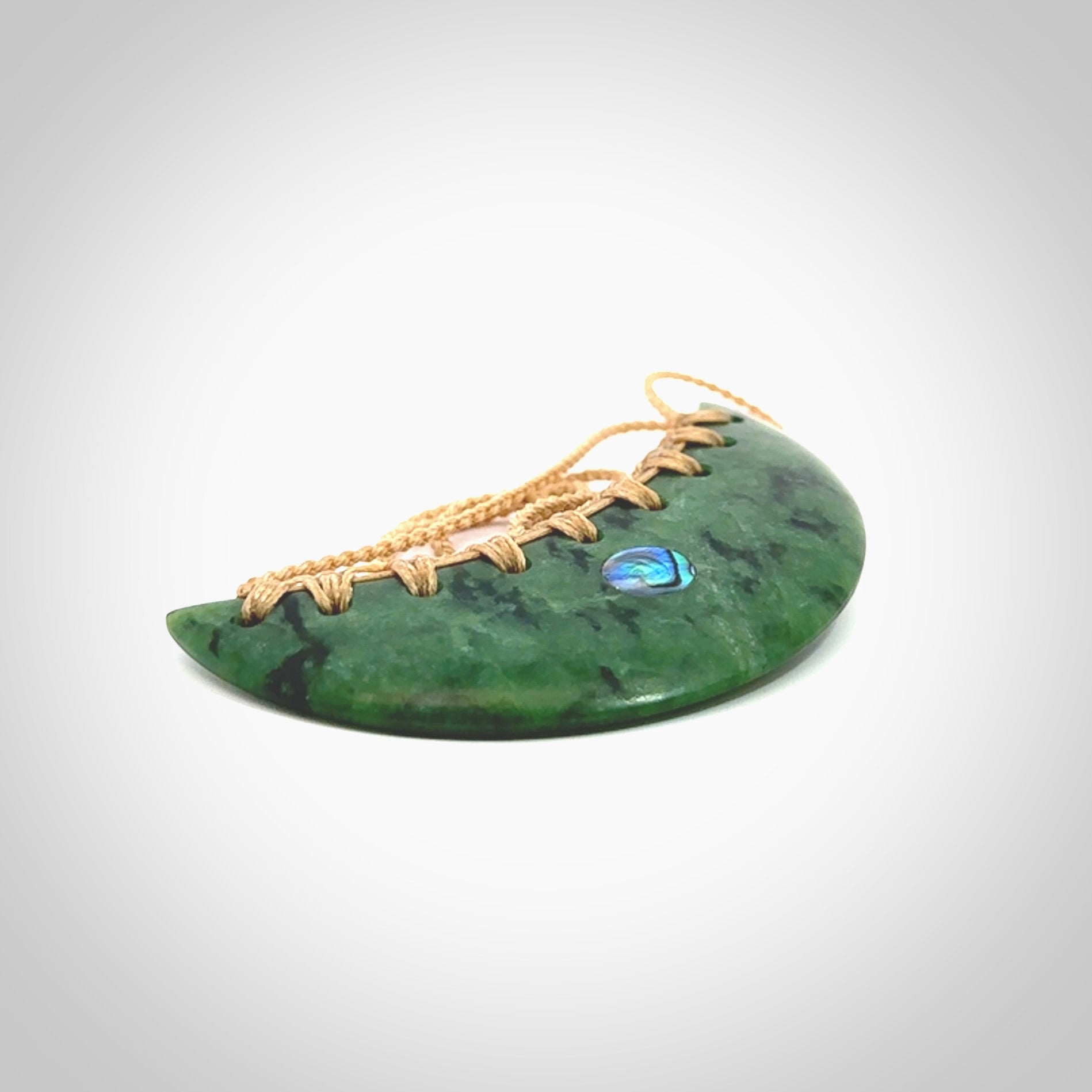 This picture shows a large hand carved jade contemporary half-shield pendant with Paua Shell inlay. It is a deep green and is a wonderful, delicate piece of jewellery. The cord is hand plaited and adjustable so that you can position the pendant where it suits you best. This piece was carved for us by Kyohei Noguchi. Delivery is free worldwide.