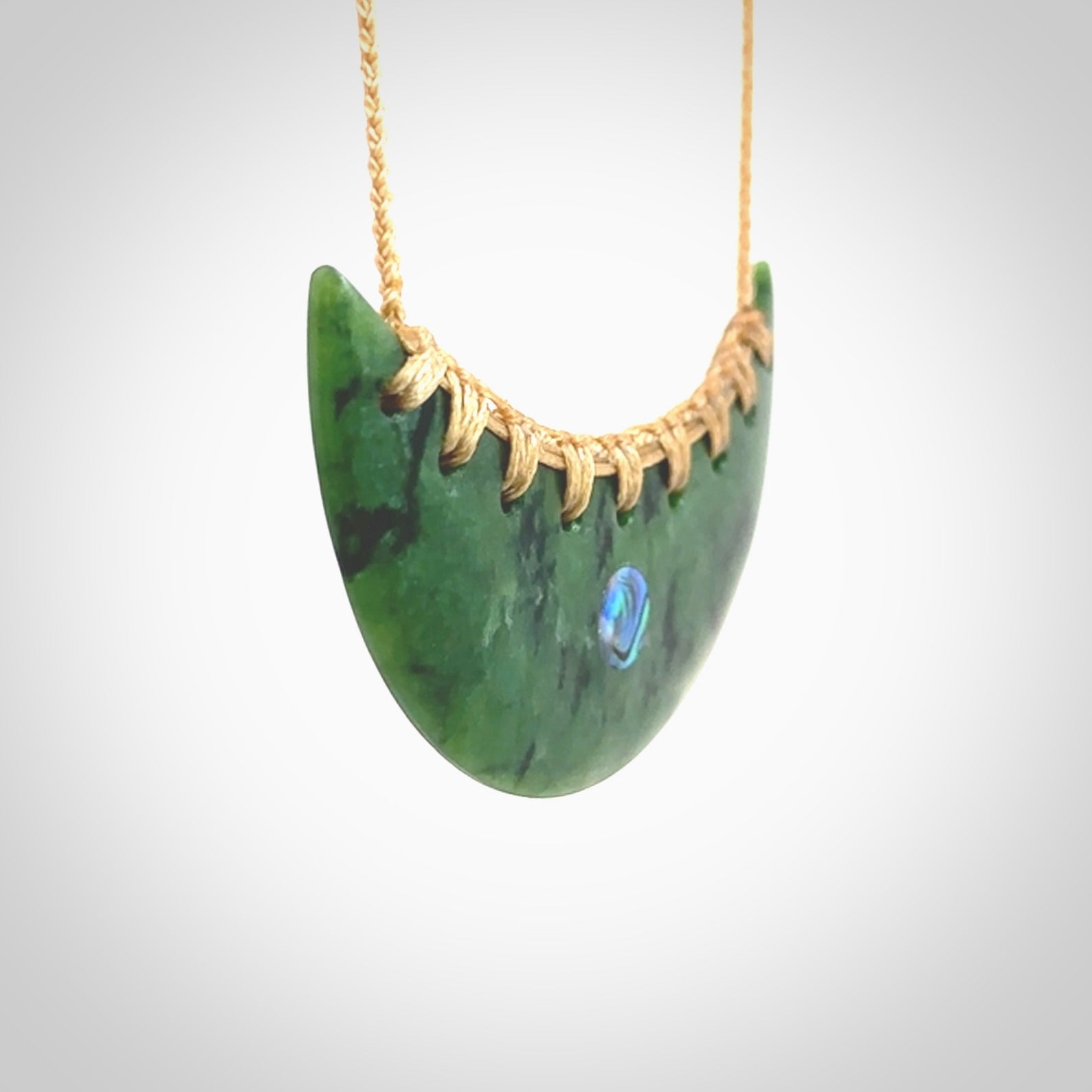 This picture shows a large hand carved jade contemporary half-shield pendant with Paua Shell inlay. It is a deep green and is a wonderful, delicate piece of jewellery. The cord is hand plaited and adjustable so that you can position the pendant where it suits you best. This piece was carved for us by Kyohei Noguchi. Delivery is free worldwide.