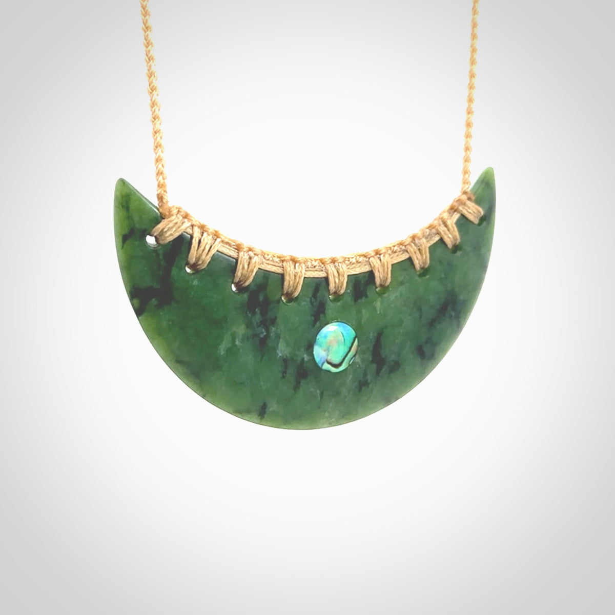 This picture shows a large hand carved jade contemporary half-shield pendant with Paua Shell inlay. It is a deep green and is a wonderful, delicate piece of jewellery. The cord is hand plaited and adjustable so that you can position the pendant where it suits you best. This piece was carved for us by Kyohei Noguchi. Delivery is free worldwide.