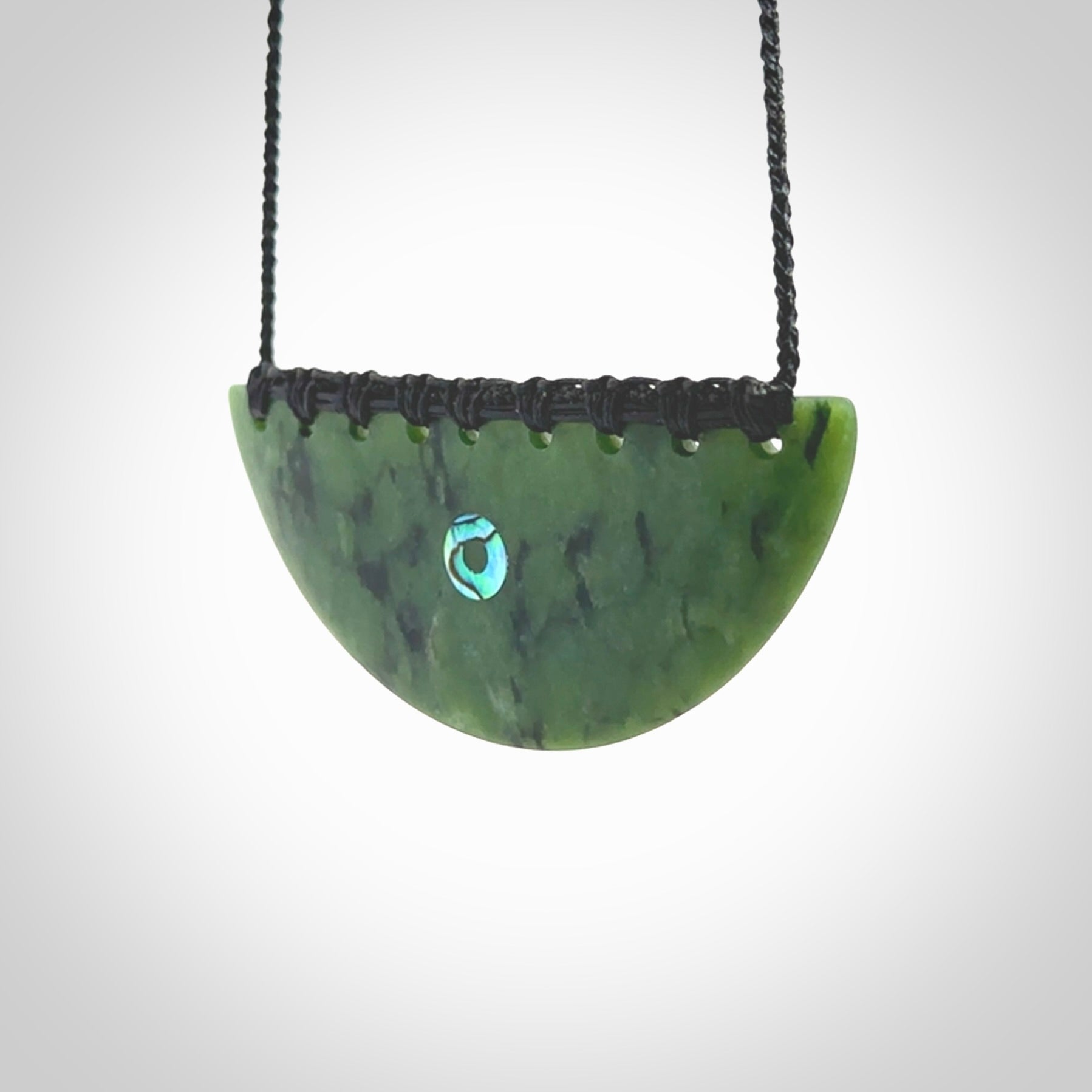 This picture shows a large hand carved jade contemporary half-shield pendant with Paua Shell inlay. It is a deep green and is a wonderful, delicate piece of jewellery. The cord is hand plaited and adjustable so that you can position the pendant where it suits you best. This piece was carved for us by Kyohei Noguchi. Delivery is free worldwide.