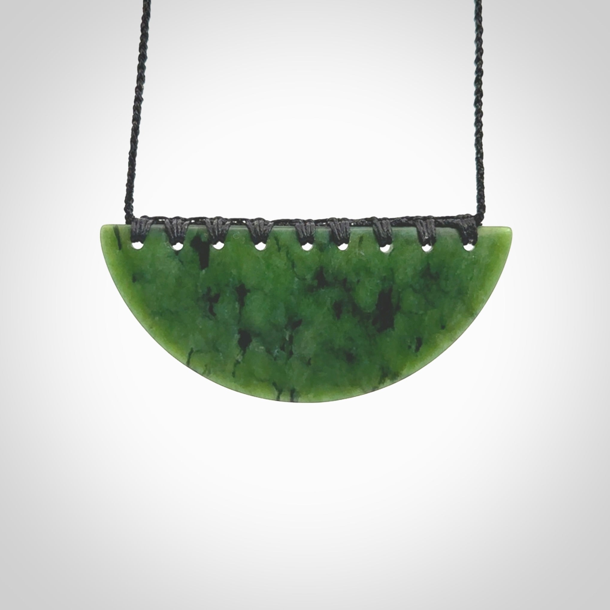 This picture shows a large hand carved jade contemporary half-shield pendant with Paua Shell inlay. It is a deep green and is a wonderful, delicate piece of jewellery. The cord is hand plaited and adjustable so that you can position the pendant where it suits you best. This piece was carved for us by Kyohei Noguchi. Delivery is free worldwide.