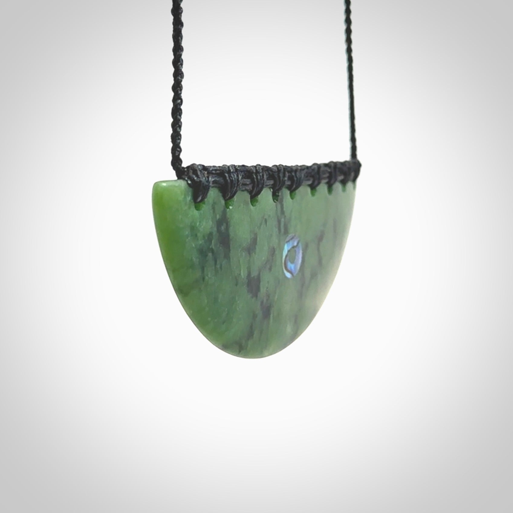 This picture shows a large hand carved jade contemporary half-shield pendant with Paua Shell inlay. It is a deep green and is a wonderful, delicate piece of jewellery. The cord is hand plaited and adjustable so that you can position the pendant where it suits you best. This piece was carved for us by Kyohei Noguchi. Delivery is free worldwide.