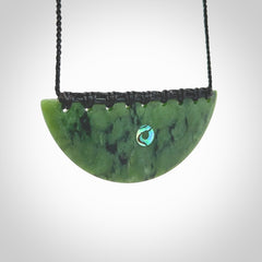 This picture shows a large hand carved jade contemporary half-shield pendant with Paua Shell inlay. It is a deep green and is a wonderful, delicate piece of jewellery. The cord is hand plaited and adjustable so that you can position the pendant where it suits you best. This piece was carved for us by Kyohei Noguchi. Delivery is free worldwide.