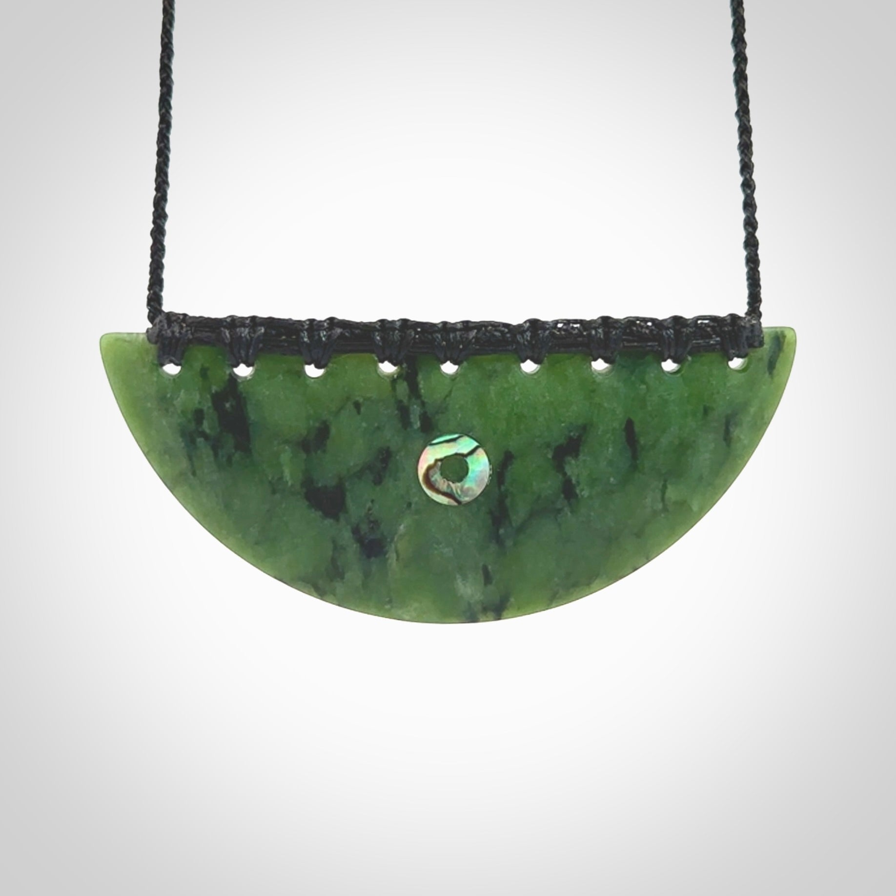 This picture shows a large hand carved jade contemporary half-shield pendant with Paua Shell inlay. It is a deep green and is a wonderful, delicate piece of jewellery. The cord is hand plaited and adjustable so that you can position the pendant where it suits you best. This piece was carved for us by Kyohei Noguchi. Delivery is free worldwide.