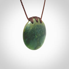 This piece is a medium sized, oval round, disc pendant. It was carved for us by Ric Moor from a lovely deep green and orange piece of New Zealand flower jade. It is suspended on an brown coloured braided cord that is length adjustable.