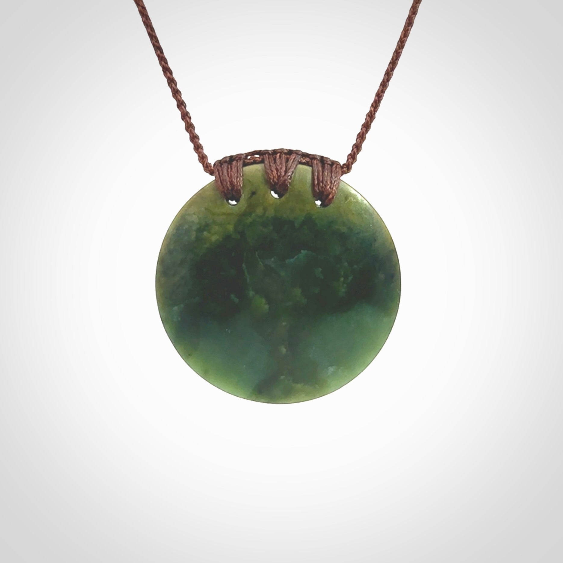 This piece is a medium sized, oval round, disc pendant. It was carved for us by Ric Moor from a lovely deep green and orange piece of New Zealand flower jade. It is suspended on an brown coloured braided cord that is length adjustable.