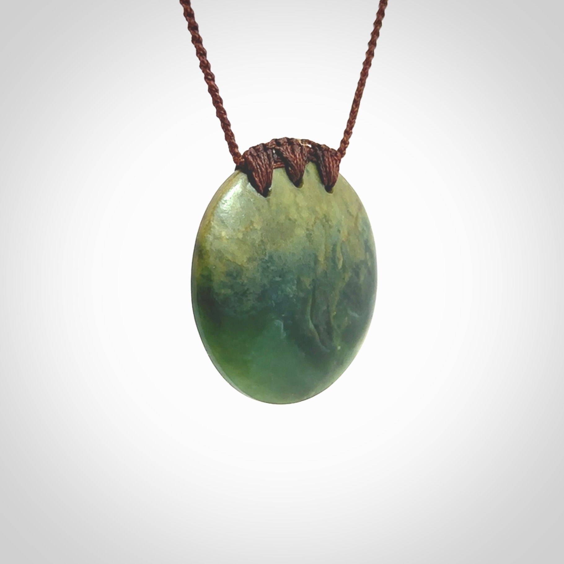 This piece is a medium sized, oval round, disc pendant. It was carved for us by Ric Moor from a lovely deep green and orange piece of New Zealand flower jade. It is suspended on an brown coloured braided cord that is length adjustable.