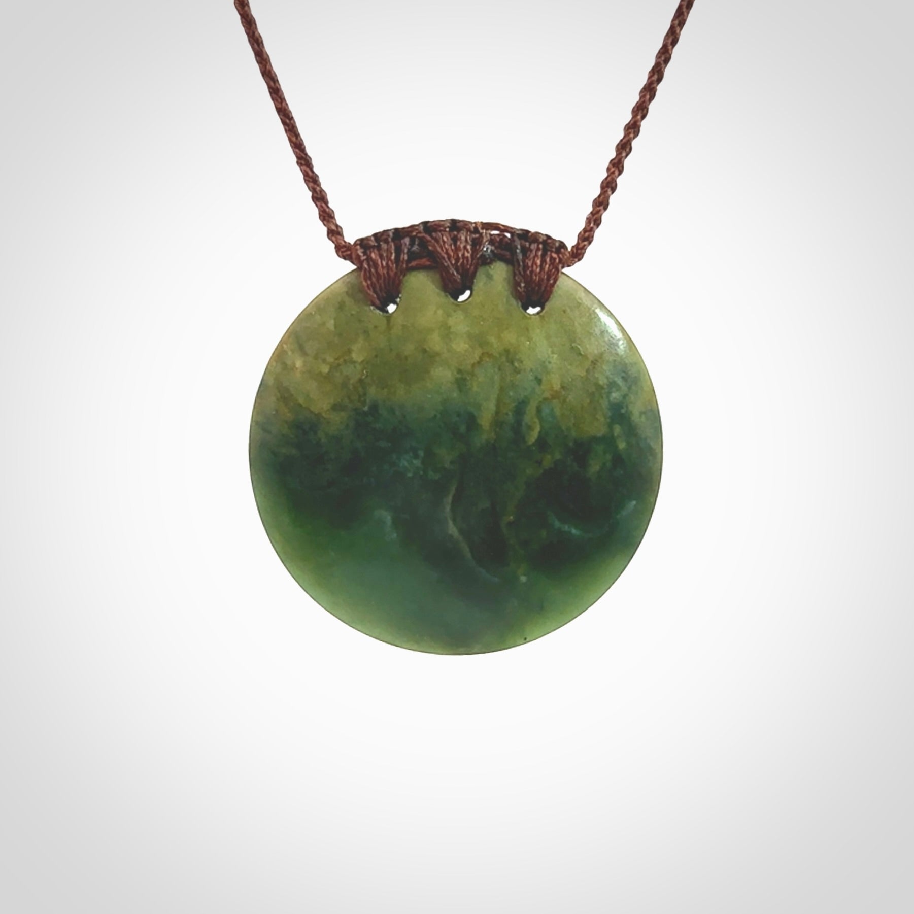 This piece is a medium sized, oval round, disc pendant. It was carved for us by Ric Moor from a lovely deep green and orange piece of New Zealand flower jade. It is suspended on an brown coloured braided cord that is length adjustable.