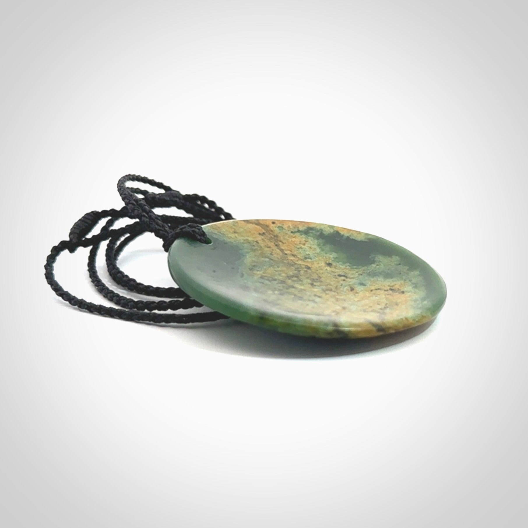 This piece is a large oval round, disc pendant. It was carved for us by Ric Moor from a lovely orange and green piece of New Zealand flower jade. It is suspended on a black coloured braided cord that is length adjustable.