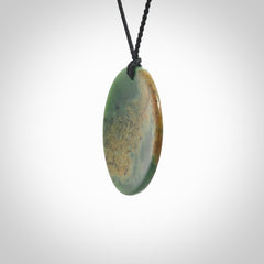 This piece is a large oval round, disc pendant. It was carved for us by Ric Moor from a lovely orange and green piece of New Zealand flower jade. It is suspended on a black coloured braided cord that is length adjustable.