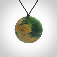 This piece is a large oval round, disc pendant. It was carved for us by Ric Moor from a lovely orange and green piece of New Zealand flower jade. It is suspended on a black coloured braided cord that is length adjustable.