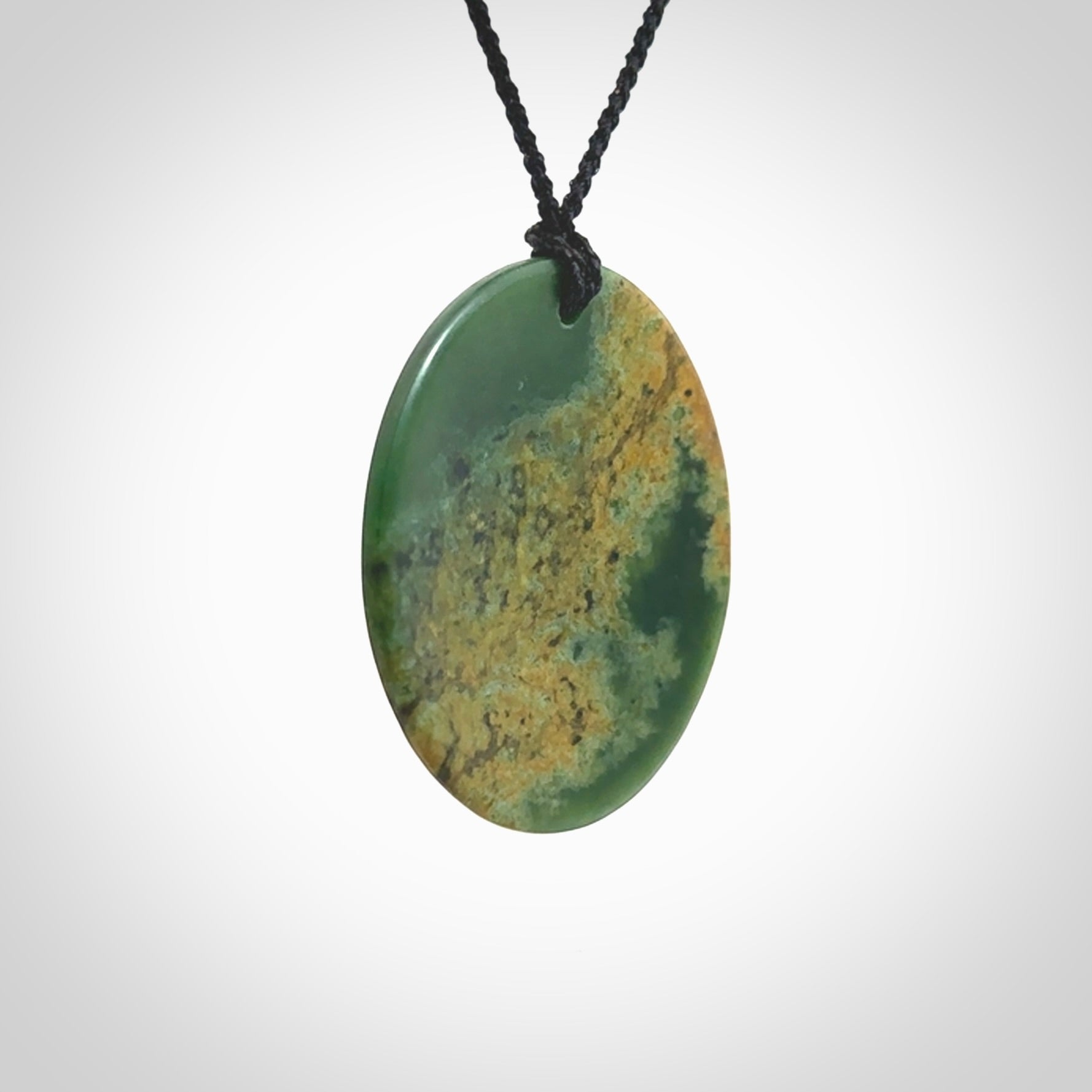 This piece is a large oval round, disc pendant. It was carved for us by Ric Moor from a lovely orange and green piece of New Zealand flower jade. It is suspended on a black coloured braided cord that is length adjustable.