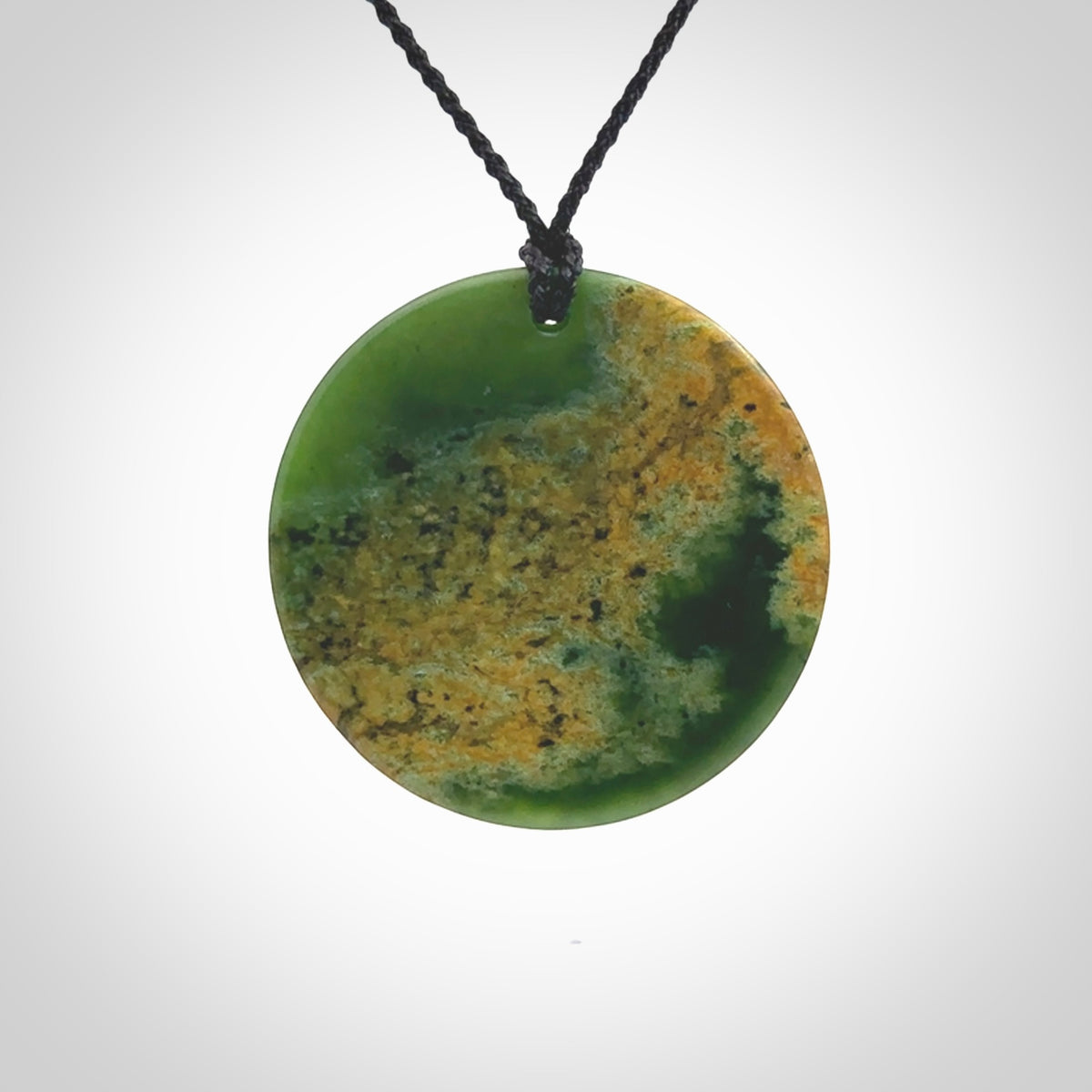 This piece is a large oval round, disc pendant. It was carved for us by Ric Moor from a lovely orange and green piece of New Zealand flower jade. It is suspended on a black coloured braided cord that is length adjustable.