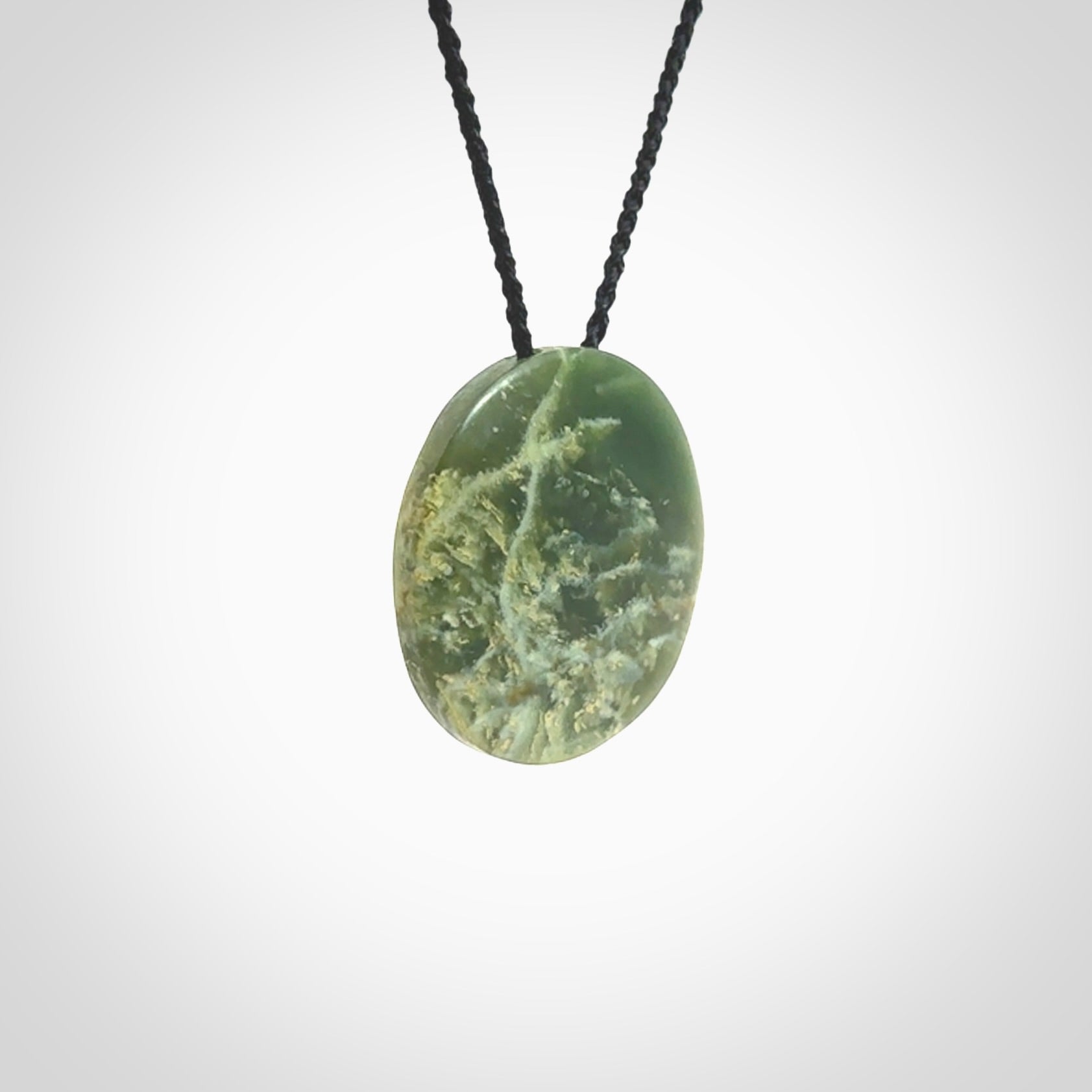 This piece is a oval round, disc pendant. It was carved for us by Ric Moor from an exquisite piece of New Zealand jade. It is suspended on a black coloured braided cord that is length adjustable.