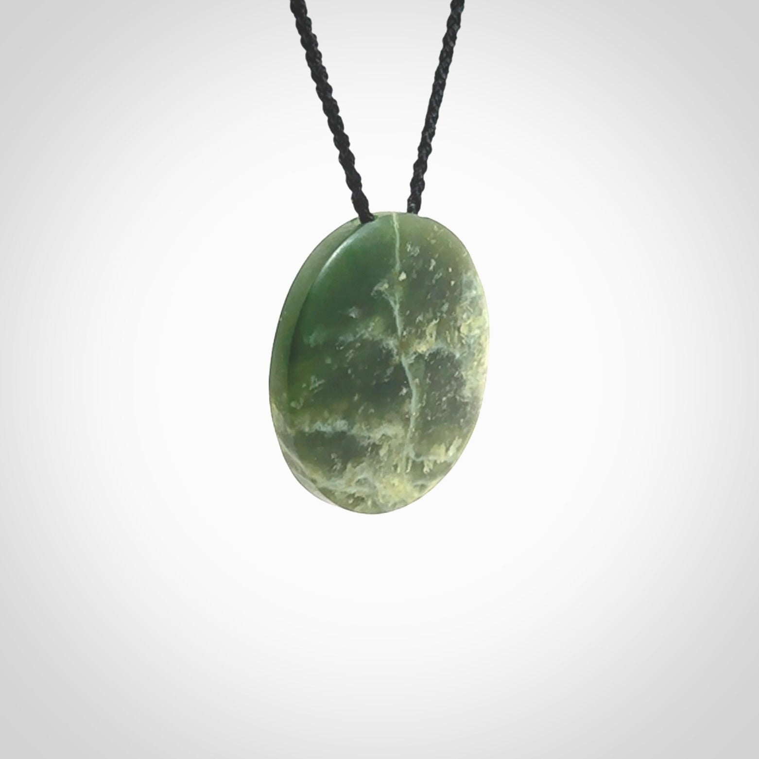 This piece is a oval round, disc pendant. It was carved for us by Ric Moor from an exquisite piece of New Zealand jade. It is suspended on a black coloured braided cord that is length adjustable.