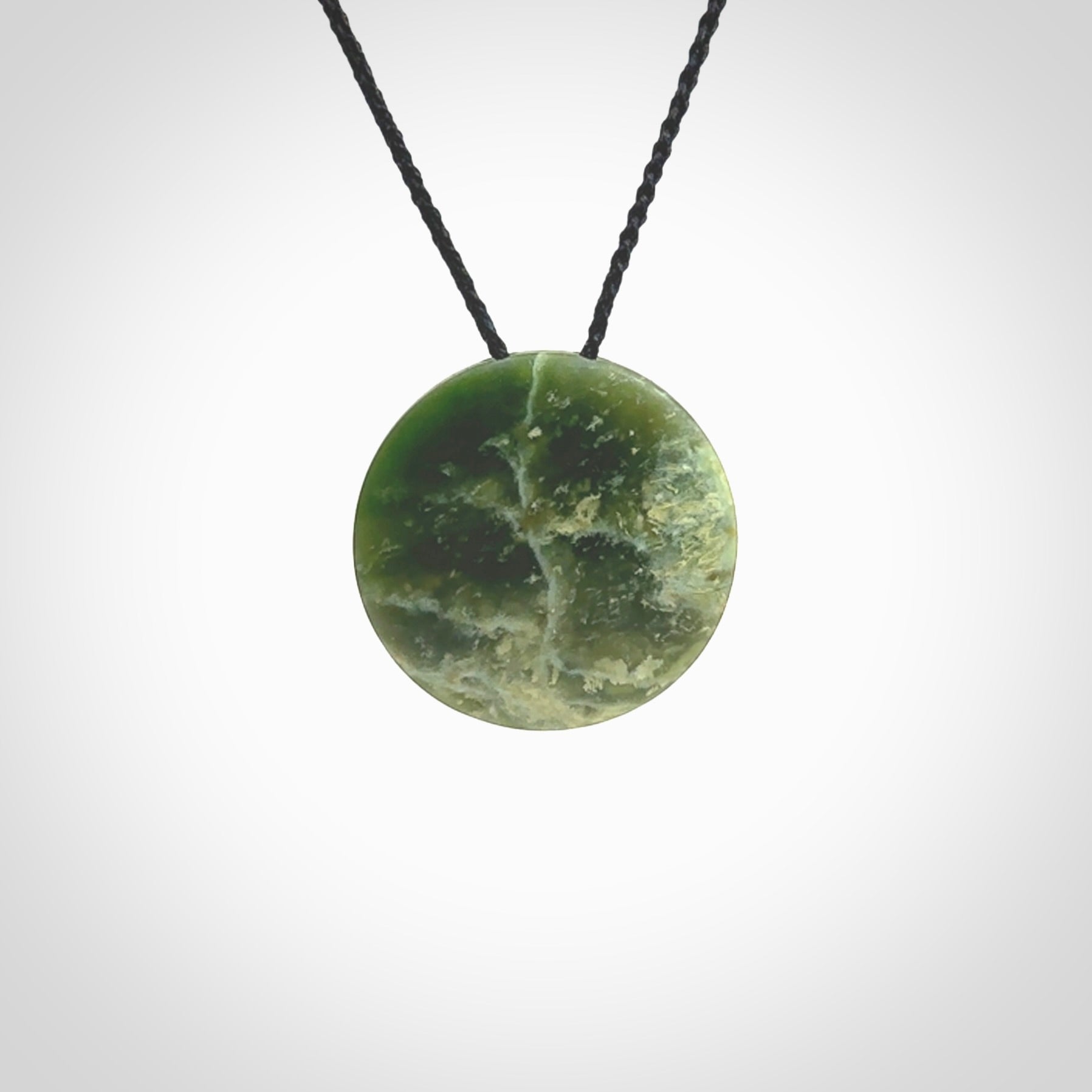 This piece is a oval round, disc pendant. It was carved for us by Ric Moor from an exquisite piece of New Zealand jade. It is suspended on a black coloured braided cord that is length adjustable.