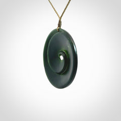 This is a large green New Zealand jade cupped koru pendant. We have bound this with a khaki coloured cord necklace. The necklace is adjustable so you can position the piece where it suits you the best. Hand made by Ric Moor.