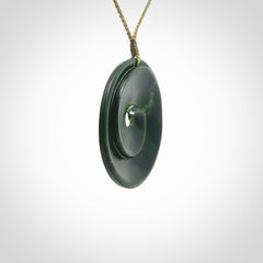 This is a large green New Zealand jade cupped koru pendant. We have bound this with a khaki coloured cord necklace. The necklace is adjustable so you can position the piece where it suits you the best. Hand made by Ric Moor.