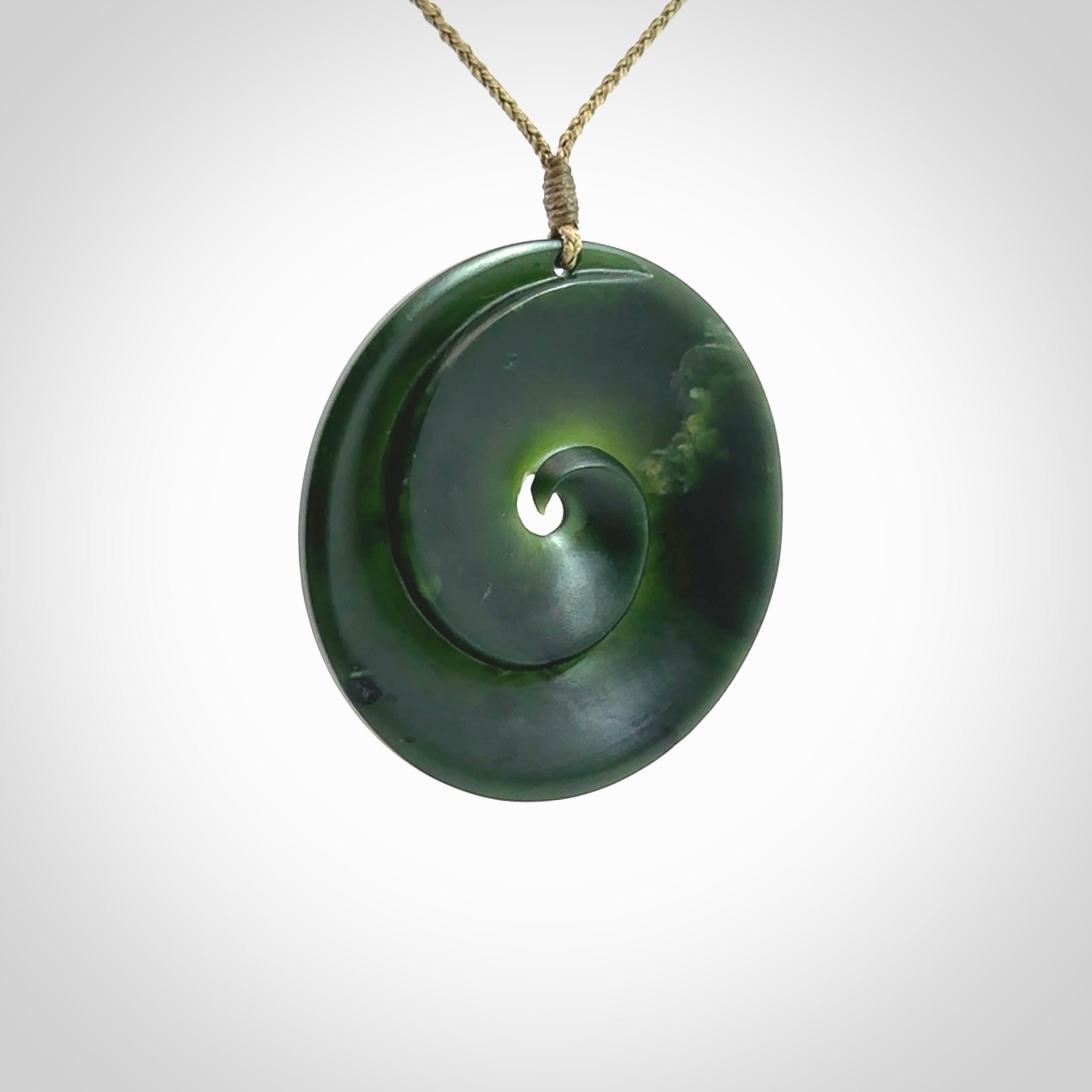 This is a large green New Zealand jade cupped koru pendant. We have bound this with a khaki coloured cord necklace. The necklace is adjustable so you can position the piece where it suits you the best. Hand made by Ric Moor.