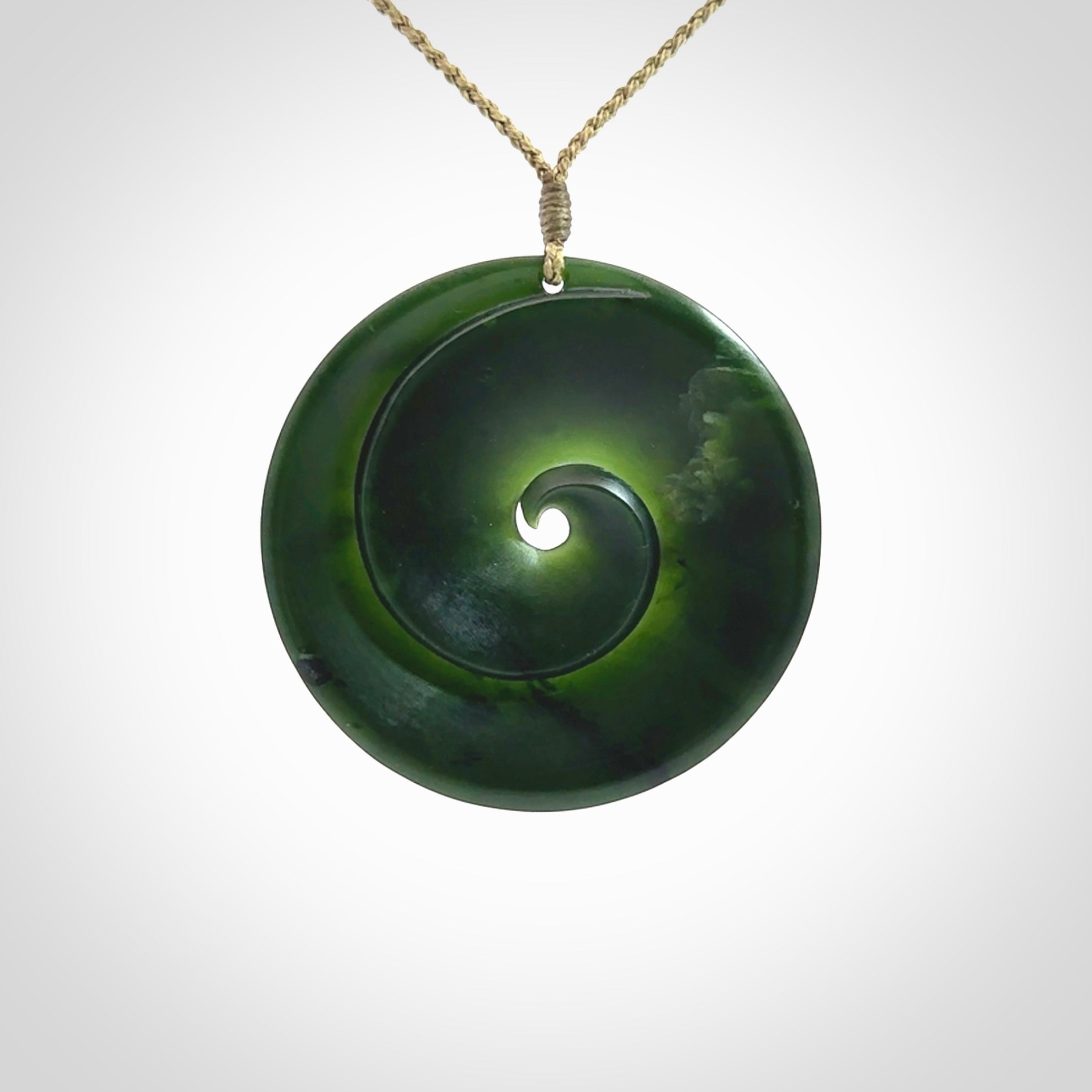 This is a large green New Zealand jade cupped koru pendant. We have bound this with a khaki coloured cord necklace. The necklace is adjustable so you can position the piece where it suits you the best. Hand made by Ric Moor.