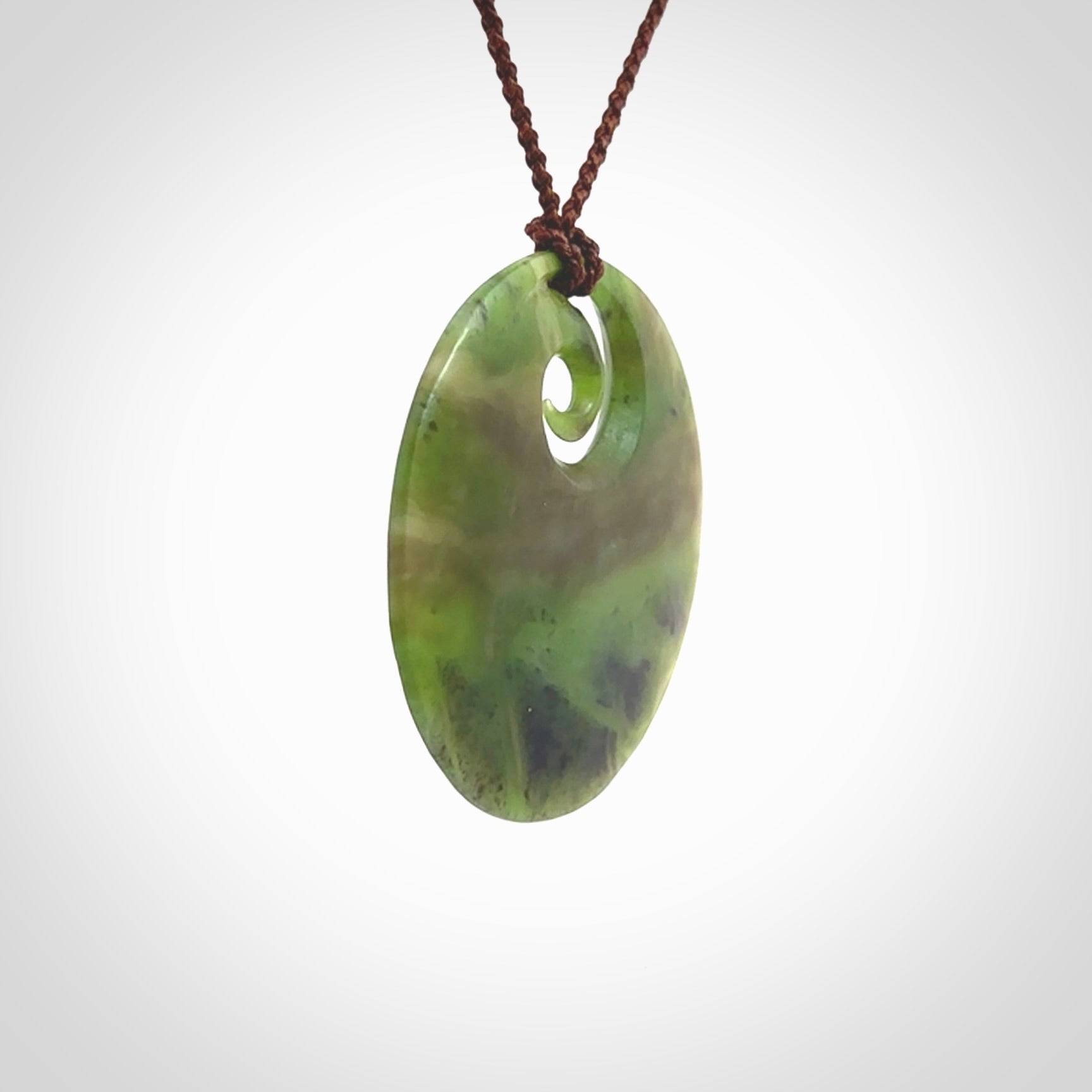 This picture shows a hand carved jade koru pendant. It is a semi-translucent green colour and is a wonderful, large sized piece of jewellery. The cord is a four plait brown colour and adjustable so that you can position the pendant where it suits you best. This koru was carved for us by Ric Moor. Delivery is free worldwide.