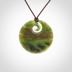 This picture shows a hand carved jade koru pendant. It is a semi-translucent green colour and is a wonderful, large sized piece of jewellery. The cord is a four plait brown colour and adjustable so that you can position the pendant where it suits you best. This koru was carved for us by Ric Moor. Delivery is free worldwide.