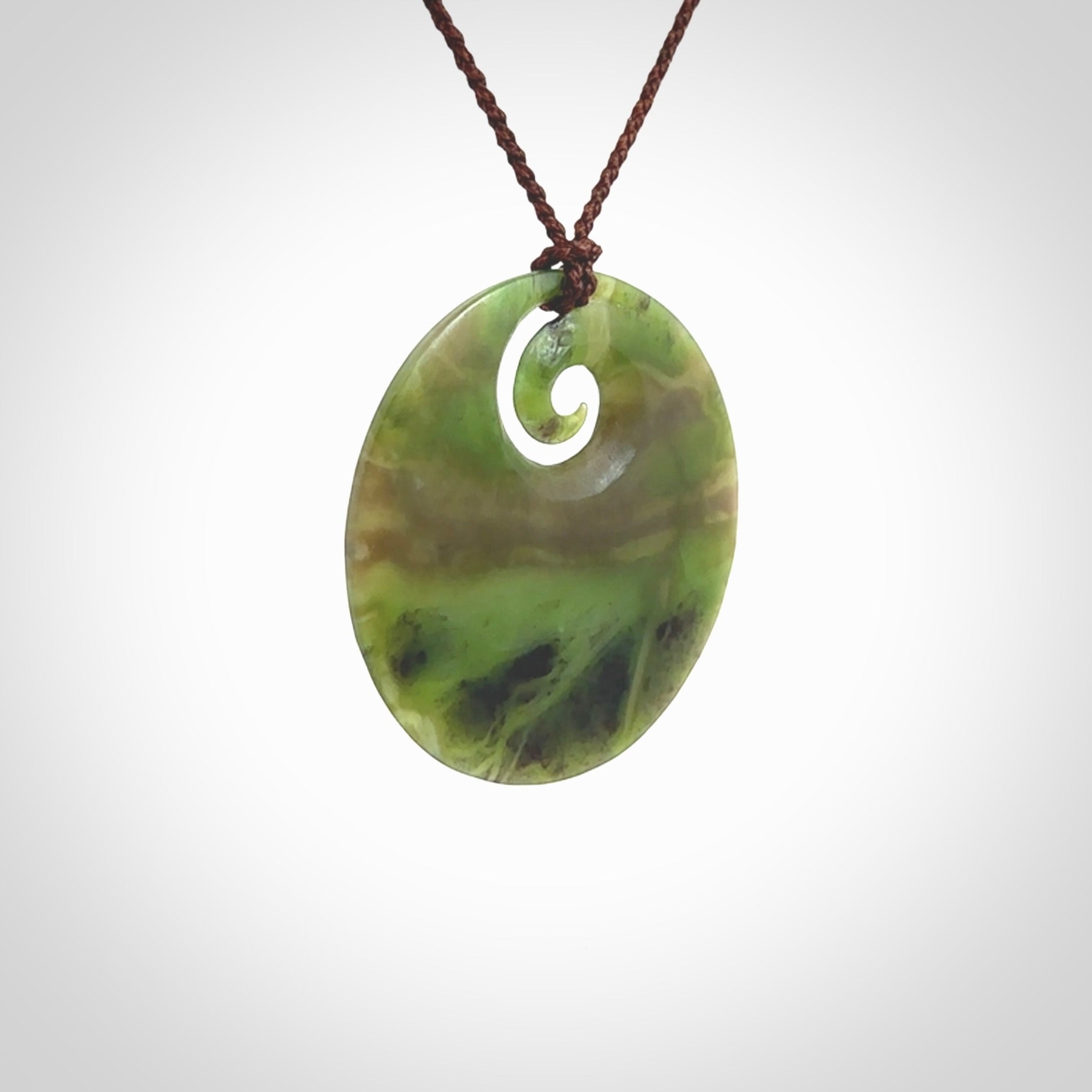 This picture shows a hand carved jade koru pendant. It is a semi-translucent green colour and is a wonderful, large sized piece of jewellery. The cord is a four plait brown colour and adjustable so that you can position the pendant where it suits you best. This koru was carved for us by Ric Moor. Delivery is free worldwide.