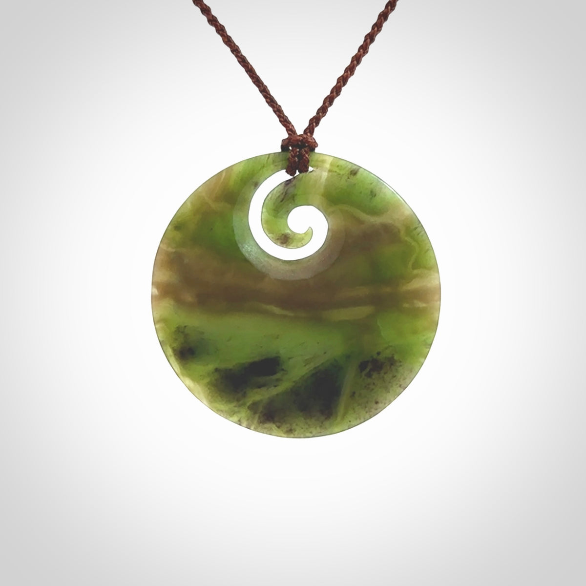 This picture shows a hand carved jade koru pendant. It is a semi-translucent green colour and is a wonderful, large sized piece of jewellery. The cord is a four plait brown colour and adjustable so that you can position the pendant where it suits you best. This koru was carved for us by Ric Moor. Delivery is free worldwide.