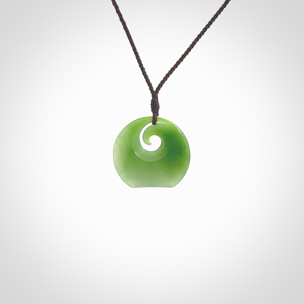 This is a small light green New Zealand Inanga jade koru pendant. We have bound this with a fine brown coloured cord necklace. The necklace is adjustable so you can position the piece where it suits you the best. Hand made by Ric Moor.