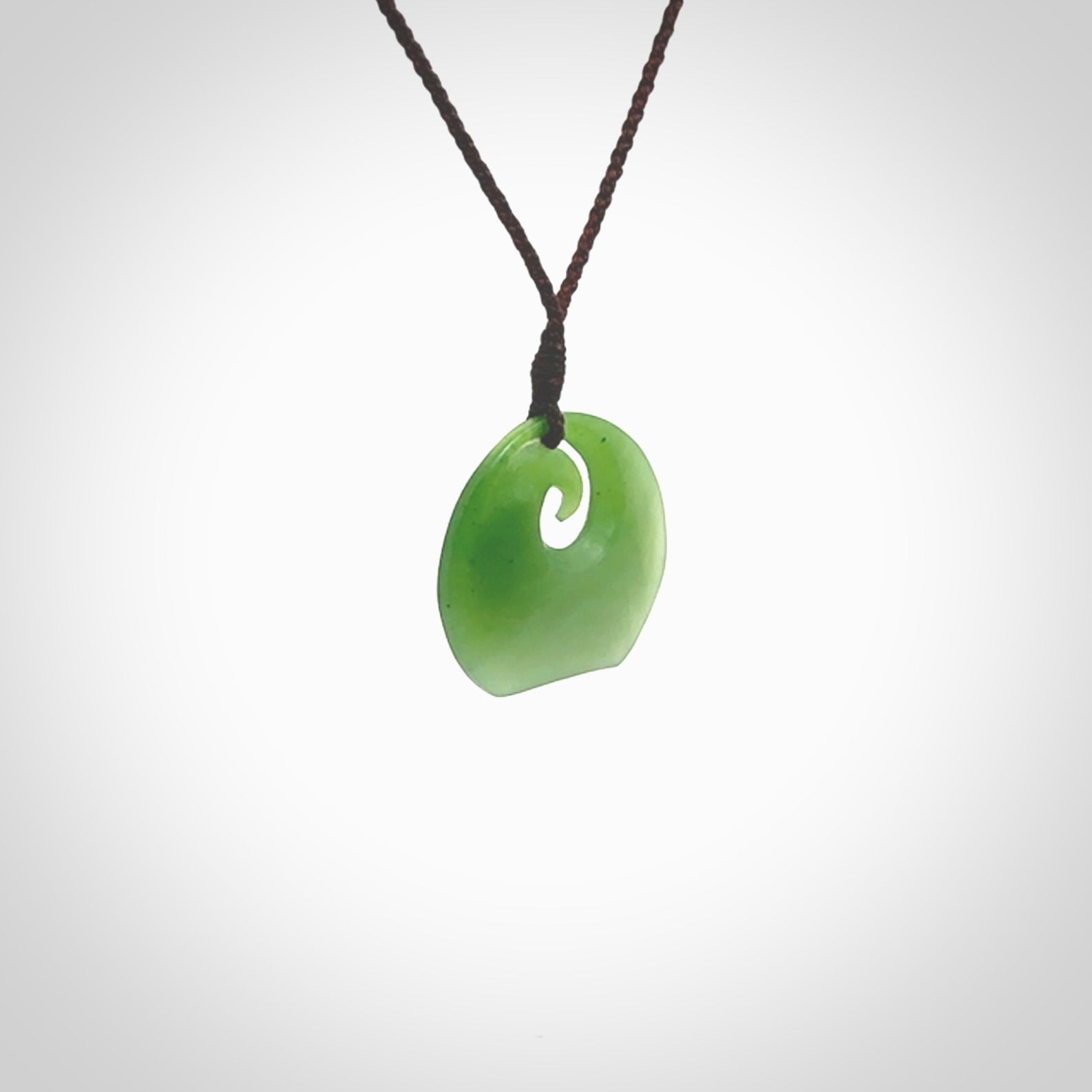 This is a small light green New Zealand Inanga jade koru pendant. We have bound this with a fine brown coloured cord necklace. The necklace is adjustable so you can position the piece where it suits you the best. Hand made by Ric Moor.