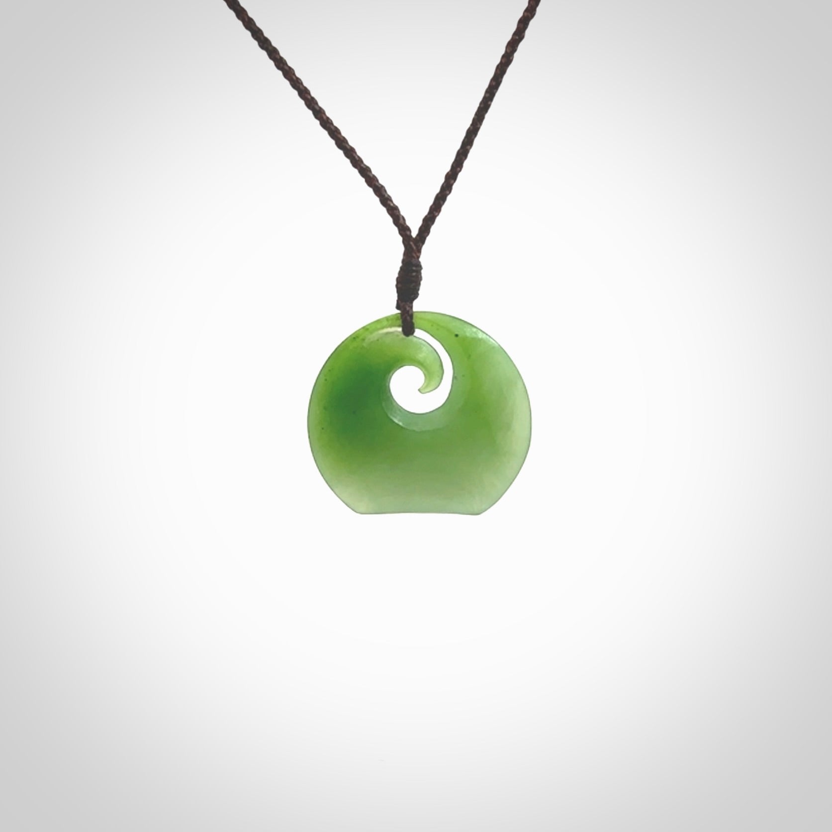 This is a small light green New Zealand Inanga jade koru pendant. We have bound this with a fine brown coloured cord necklace. The necklace is adjustable so you can position the piece where it suits you the best. Hand made by Ric Moor.