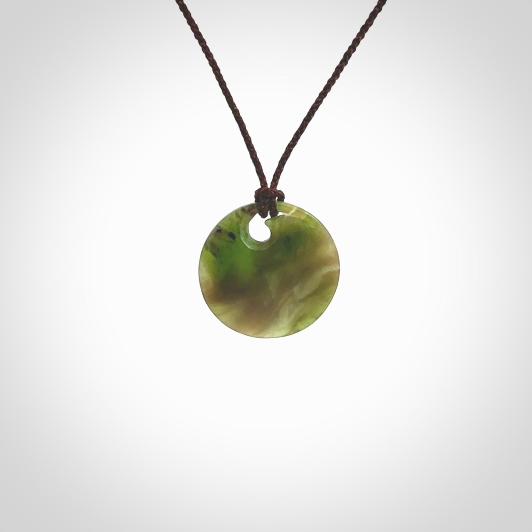 This is a small New Zealand jade koru pendant. We have bound this with a fine brown coloured cord necklace. The necklace is adjustable so you can position the piece where it suits you the best. Hand made by Ric Moor.