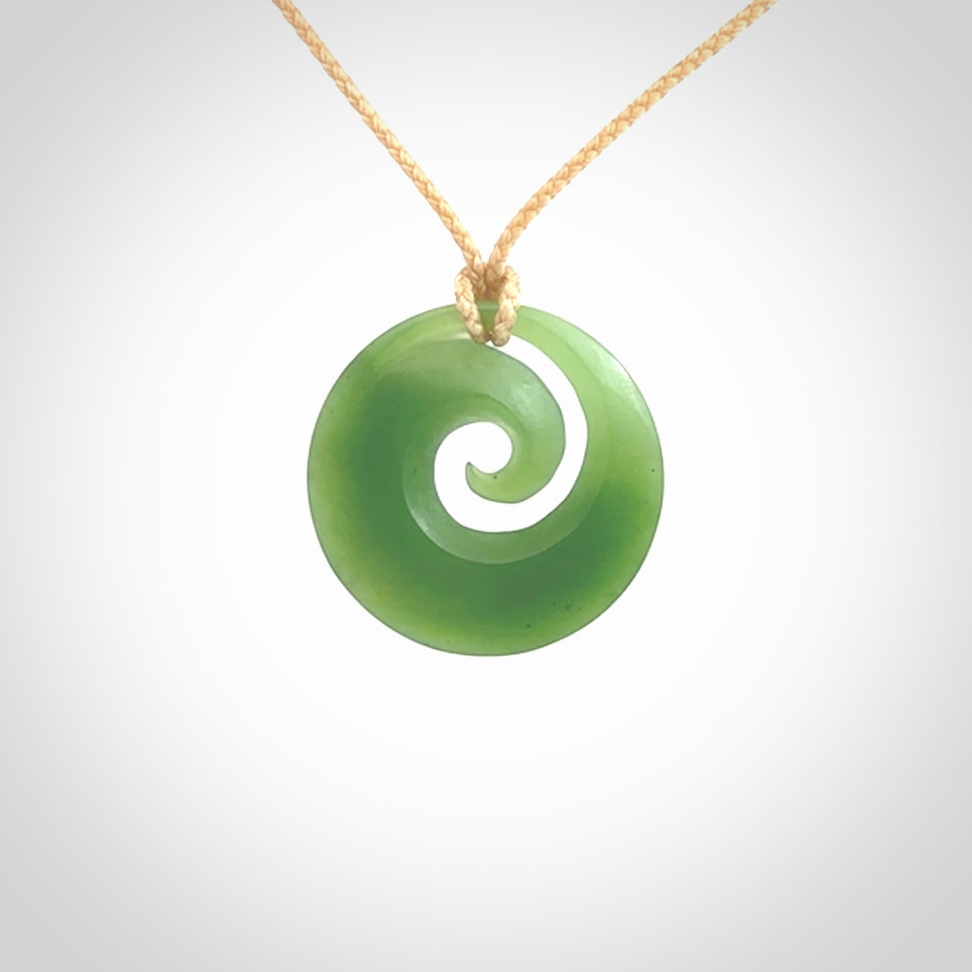 This is a small light green New Zealand Inanga jade koru pendant. We have bound this with a fine beige coloured cord necklace. The necklace is adjustable so you can position the piece where it suits you the best.