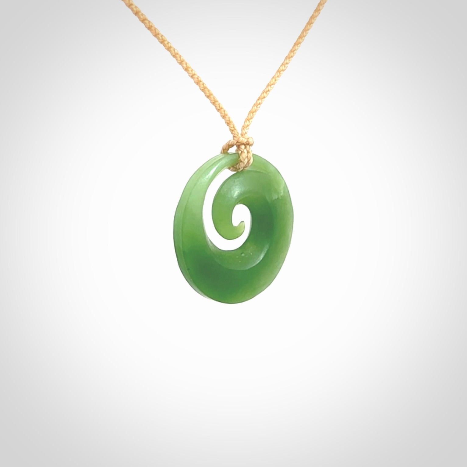 This is a small light green New Zealand Inanga jade koru pendant. We have bound this with a fine beige coloured cord necklace. The necklace is adjustable so you can position the piece where it suits you the best.