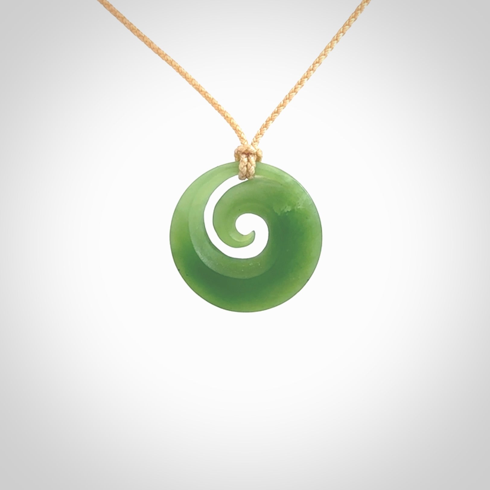 This is a small light green New Zealand Inanga jade koru pendant. We have bound this with a fine beige coloured cord necklace. The necklace is adjustable so you can position the piece where it suits you the best.