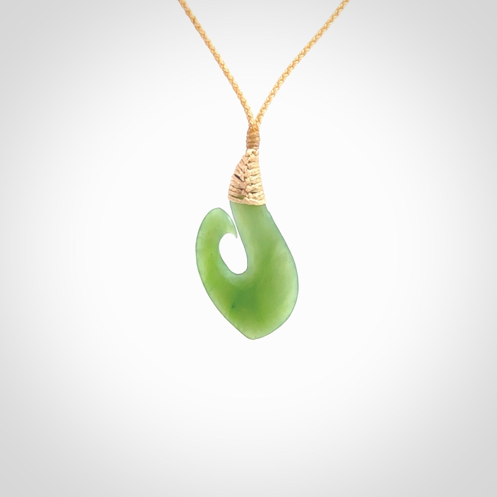 New Zealand jade hei-mate pendant. Hand carved in bright green jade by Ric Moor. The pendant is suspended from a beige plaited cord and is finished in a satin matte polish.