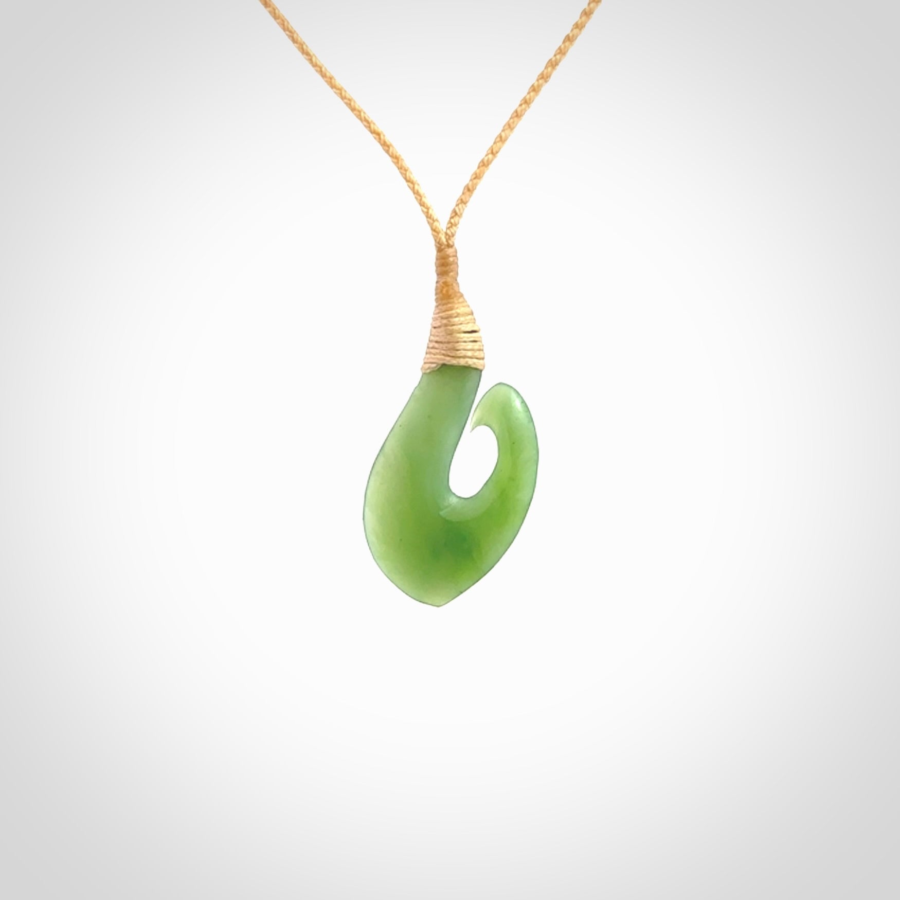 New Zealand jade hei-mate pendant. Hand carved in bright green jade by Ric Moor. The pendant is suspended from a beige plaited cord and is finished in a satin matte polish.