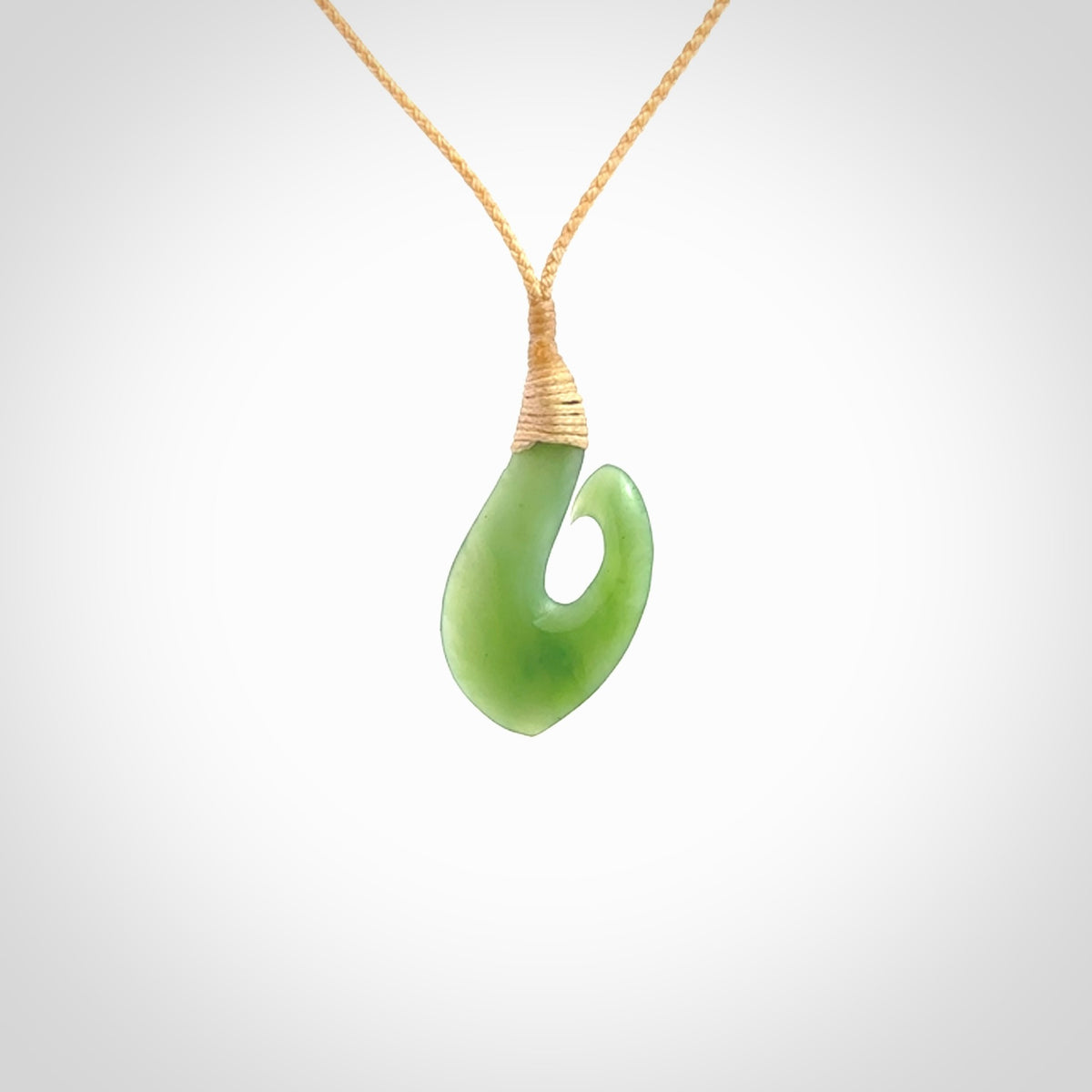 New Zealand jade hei-mate pendant. Hand carved in bright green jade by Ric Moor. The pendant is suspended from a beige plaited cord and is finished in a satin matte polish.