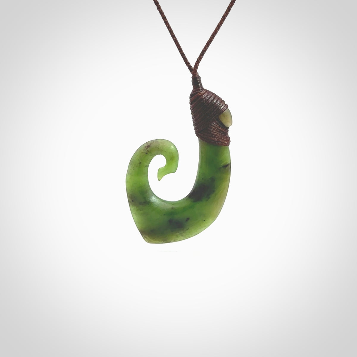 This picture shows a jade hook pendant, also called a hei-matau, carved for us in New Zealand jade. The jade is a wonderful green pounamu. This is a rare jade loved and valued for its distinctive colour. The carver is Ric Moor - and this is a beautiful example of his work. The cord is a four-plait, adjustable brown coloured necklace.