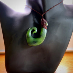 This picture shows a jade hook pendant, also called a hei-matau, carved for us in New Zealand jade. The jade is a wonderful green pounamu. This is a rare jade loved and valued for its distinctive colour. The carver is Ric Moor - and this is a beautiful example of his work. The cord is a four-plait, adjustable brown coloured necklace.