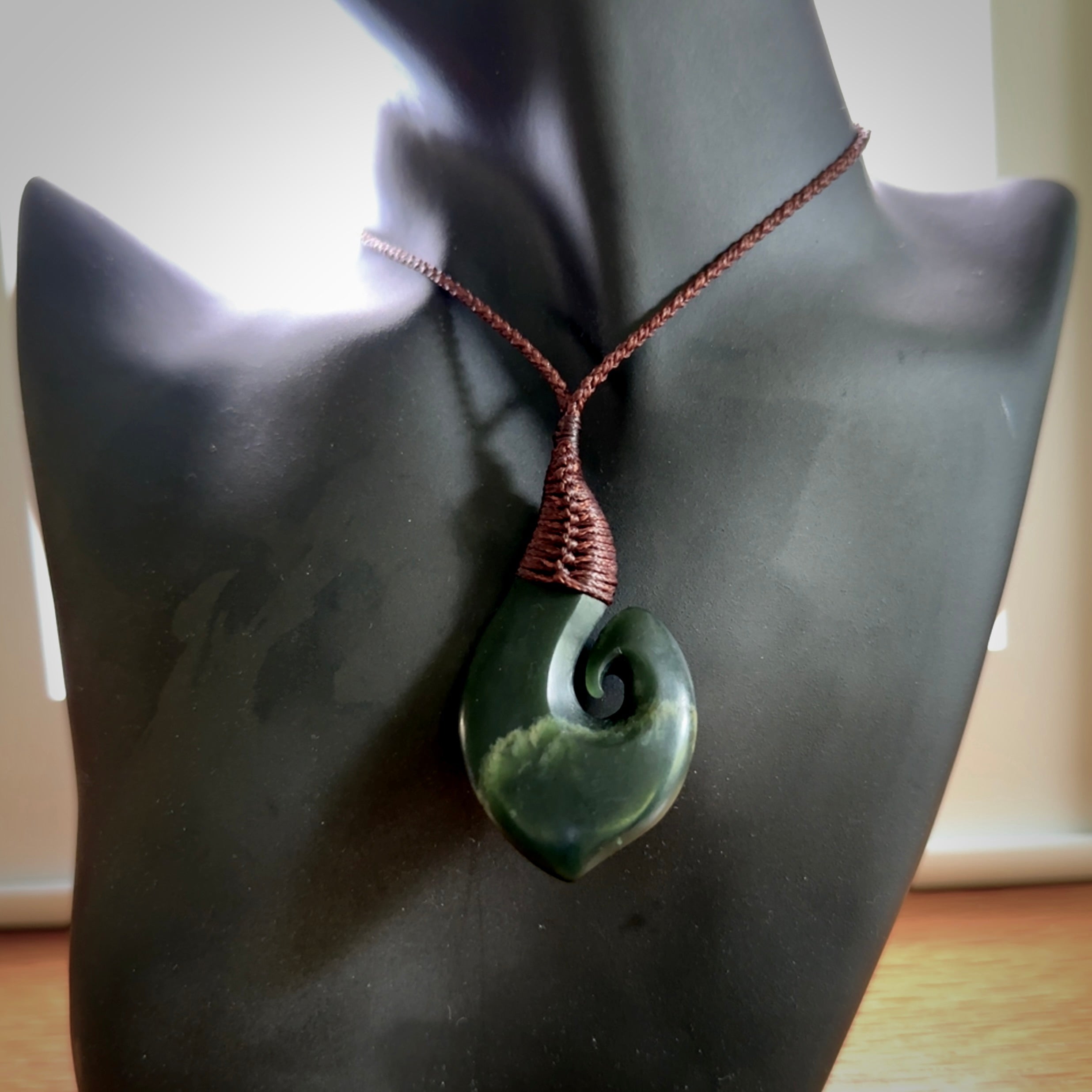 A hand carved hei-matau with koru pendant. This pendant is a green and orange colour and is finished in a polished matte. The cord is a four plait in brown and it is adjustable. Hand carved Hook with Koru pendant by Ric Moor. Delivered to you with Express Courier at no extra cost. One only necklace.