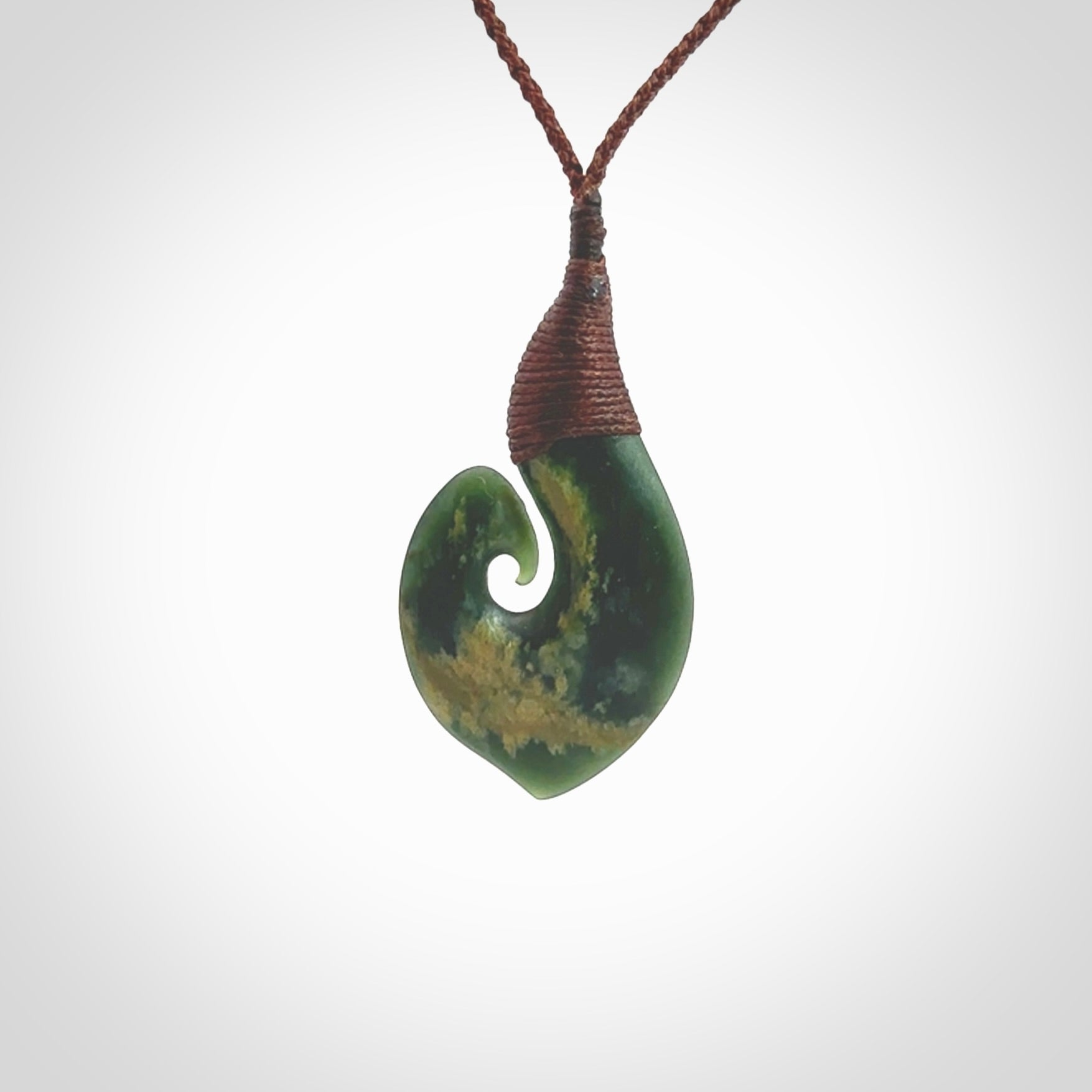 A hand carved hei-matau with koru pendant. This pendant is a green and orange colour and is finished in a polished matte. The cord is a four plait in brown and it is adjustable. Hand carved Hook with Koru pendant by Ric Moor. Delivered to you with Express Courier at no extra cost. One only necklace.