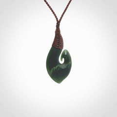 A hand carved hei-matau with koru pendant. This pendant is a green and orange colour and is finished in a polished matte. The cord is a four plait in brown and it is adjustable. Hand carved Hook with Koru pendant by Ric Moor. Delivered to you with Express Courier at no extra cost. One only necklace.