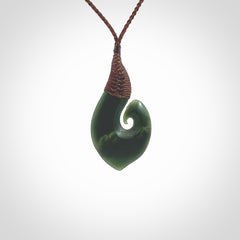 A hand carved hei-matau with koru pendant. This pendant is a green and orange colour and is finished in a polished matte. The cord is a four plait in brown and it is adjustable. Hand carved Hook with Koru pendant by Ric Moor. Delivered to you with Express Courier at no extra cost. One only necklace.