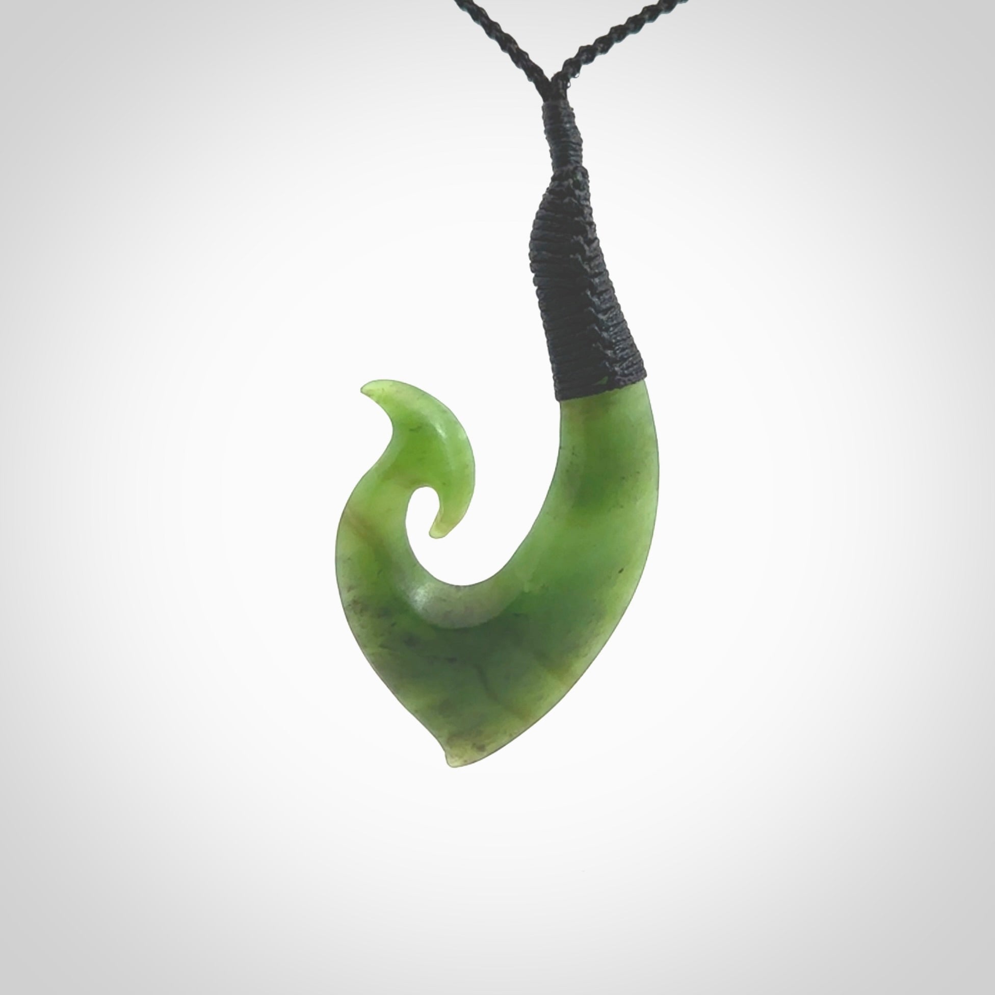 This picture shows a jade hook pendant, also called a hei-matau, carved for us in New Zealand jade. The carver is Ric Moor - and this is a beautiful example of his work. The cord is a four-plait, adjustable black coloured necklace.