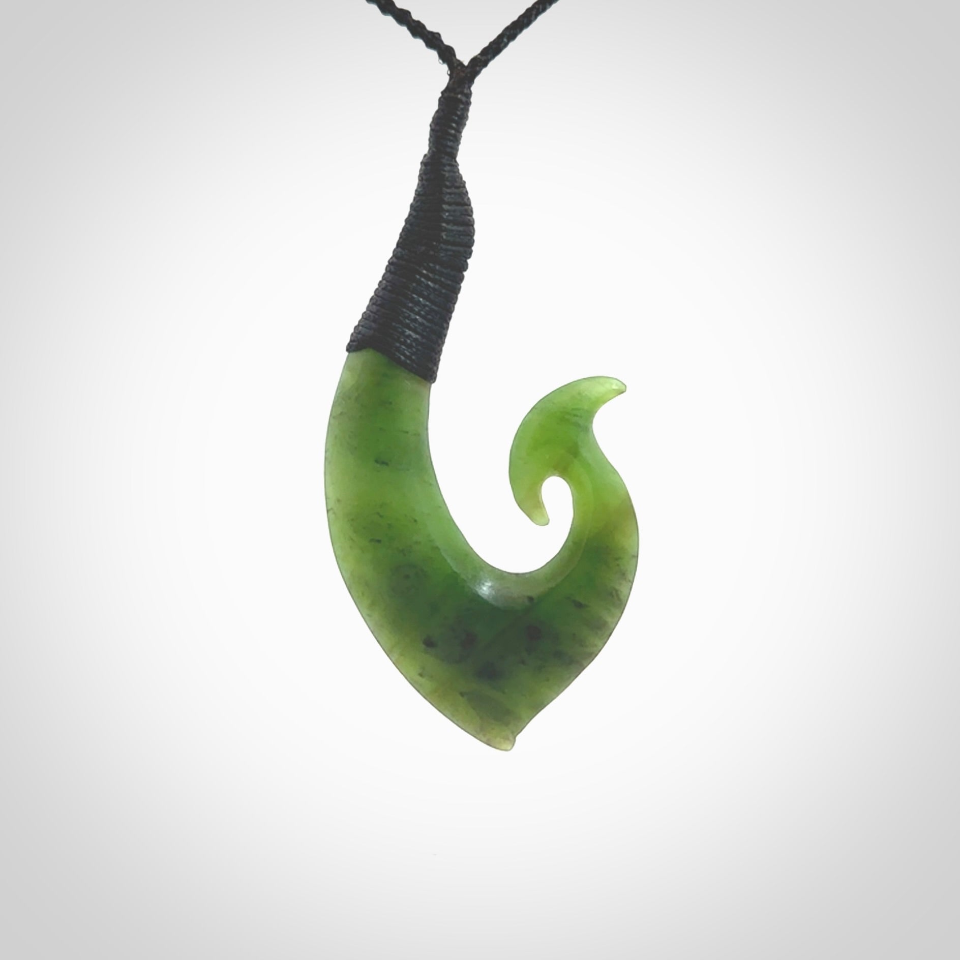 This picture shows a jade hook pendant, also called a hei-matau, carved for us in New Zealand jade. The carver is Ric Moor - and this is a beautiful example of his work. The cord is a four-plait, adjustable black coloured necklace.