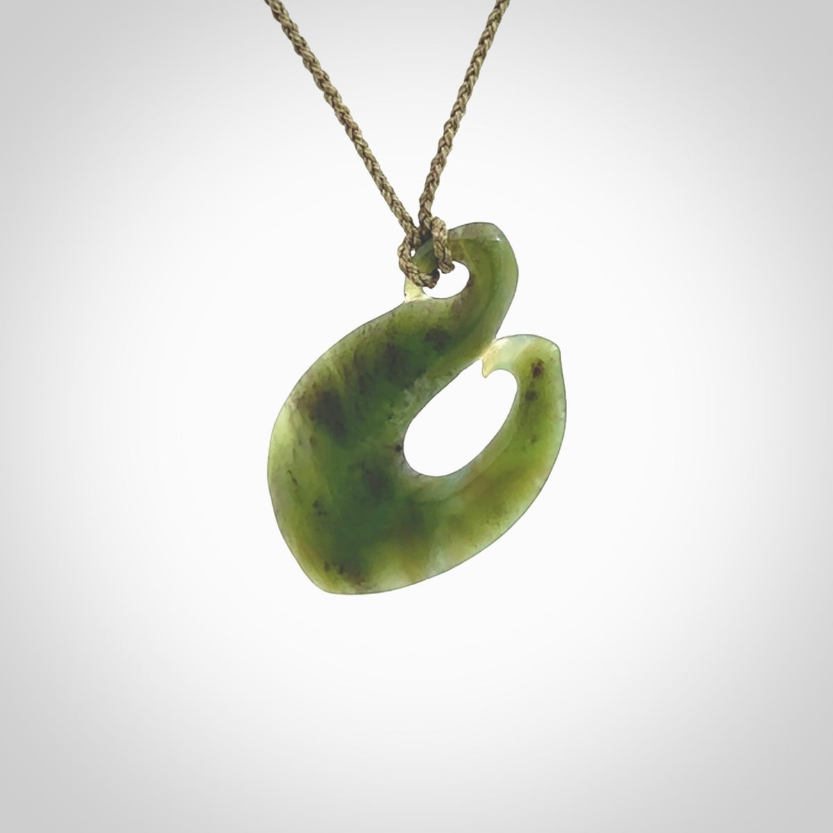 This picture shows a jade hook pendant, also called a hei-matau, carved for us in New Zealand jade. The carver is Ric Moor - and this is a beautiful example of his work. The cord is a four-plait, adjustable khaki coloured necklace.