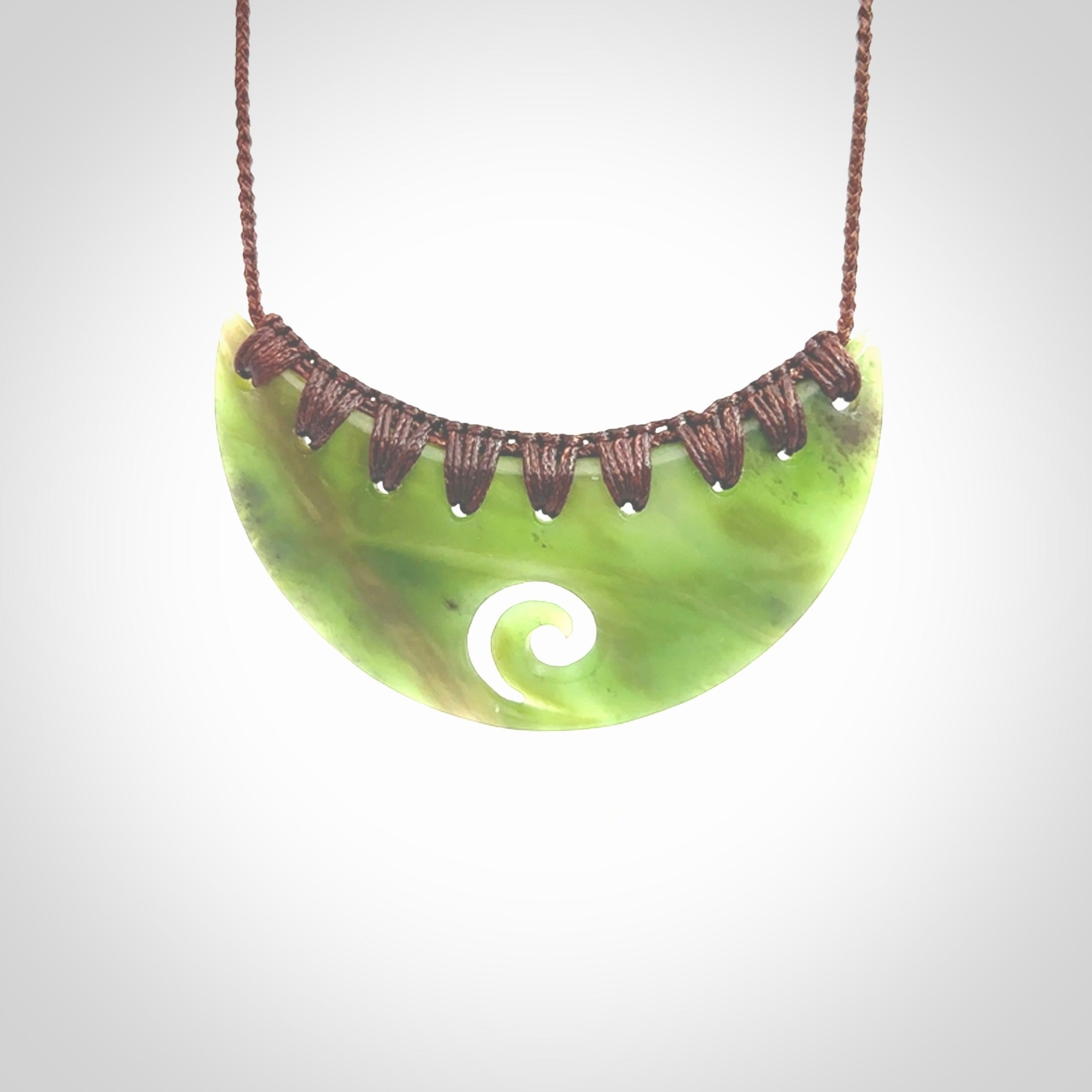 This picture shows a hand carved jade half-shield with Koru pendant. It is a semi-translucent green colour. This is a wonderful piece of jewellery. The cord is hand plaited and adjustable so that you can position the pendant where it suits you best. This piece was carved for us by Ric Moor. Delivery is free worldwide.